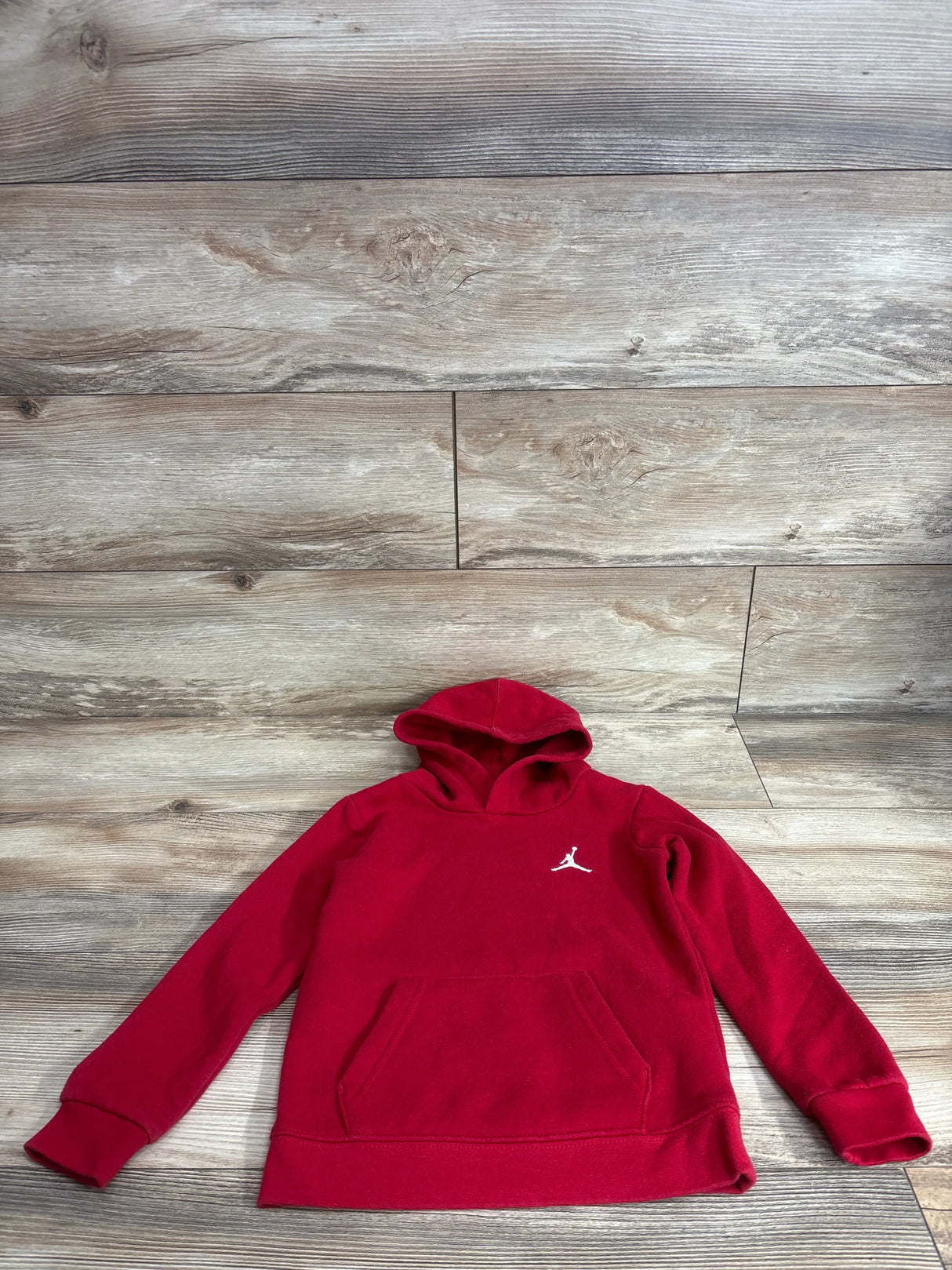 Flat lay of red Jordan pullover hoodie (toddler 4T) showing kangaroo pocket and white Jumpman logo on wood plank background