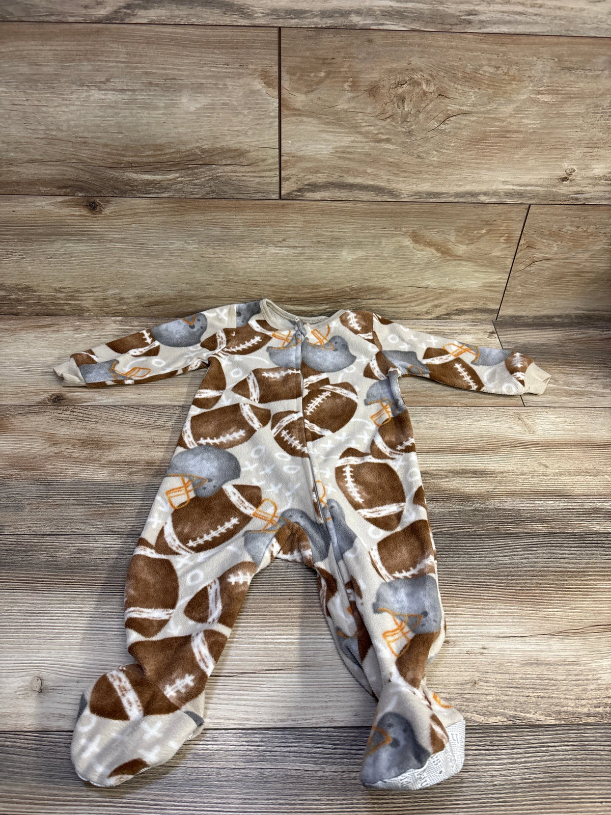 Overhead view of Kids Headquarters football blanket sleeper showcasing zip front, enclosed feet, and football helmet print on wood floor