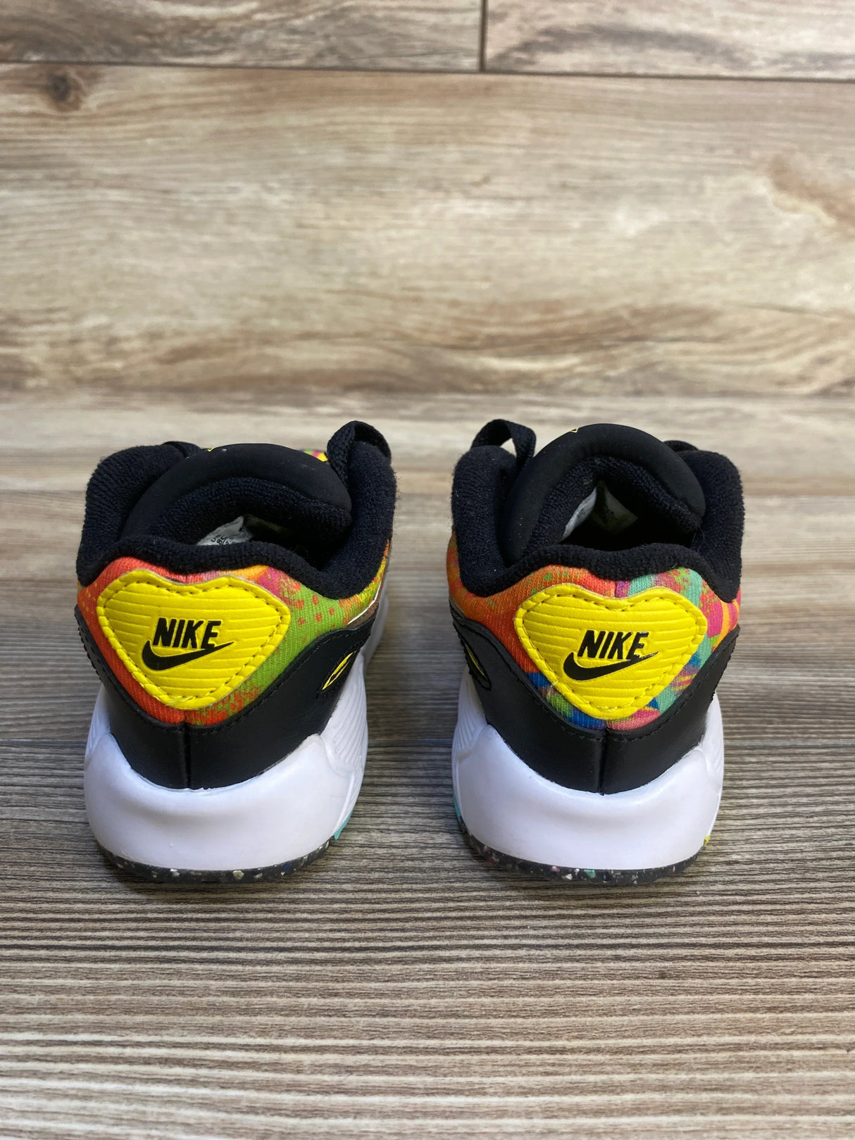 Back view of Nike Air Max 90 TD toddler sneakers size 8C showing yellow heart Nike patch and multicolor pattern on wood floor
