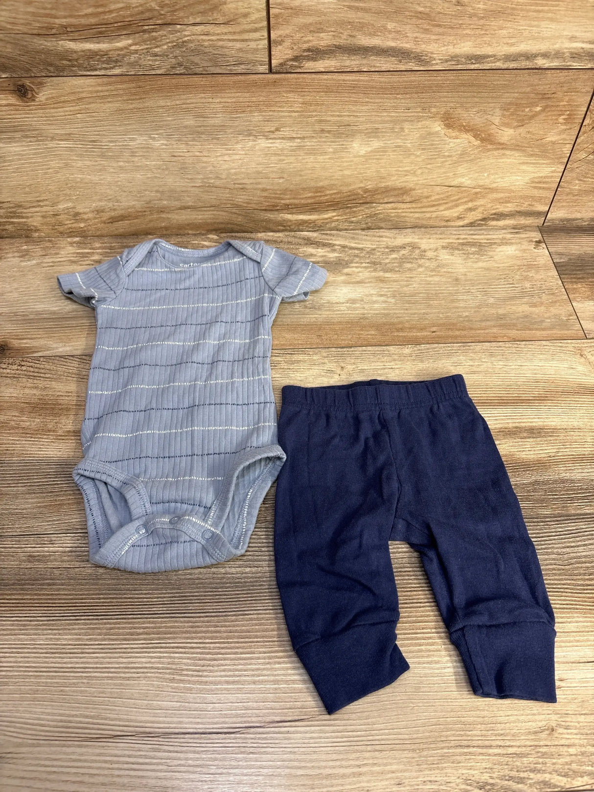 Flat lay of blue ribbed short-sleeve bodysuit with silver horizontal stripes and navy elastic-waist pants, size 3 months on wood background