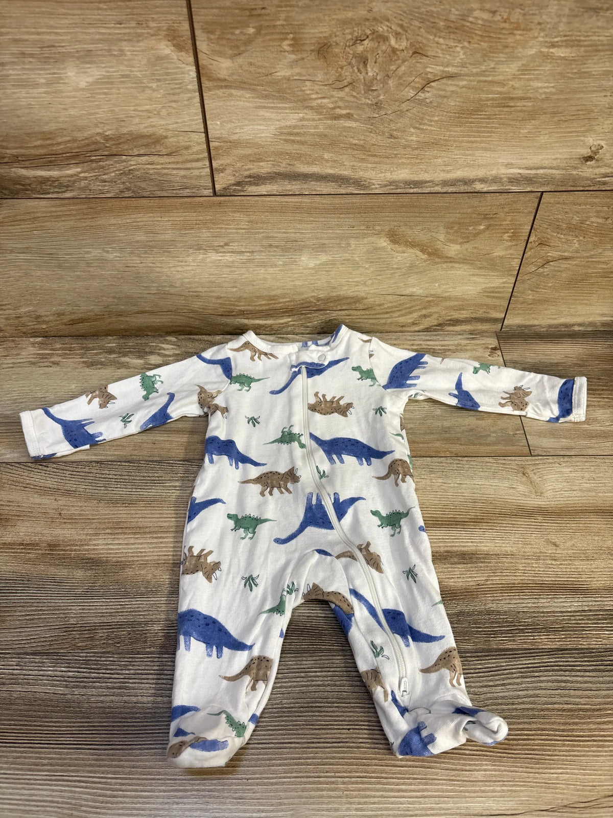 Front view of Just One You dinosaur sleeper showcasing white cotton fabric dinosaur print and two way zipper on wood flooring