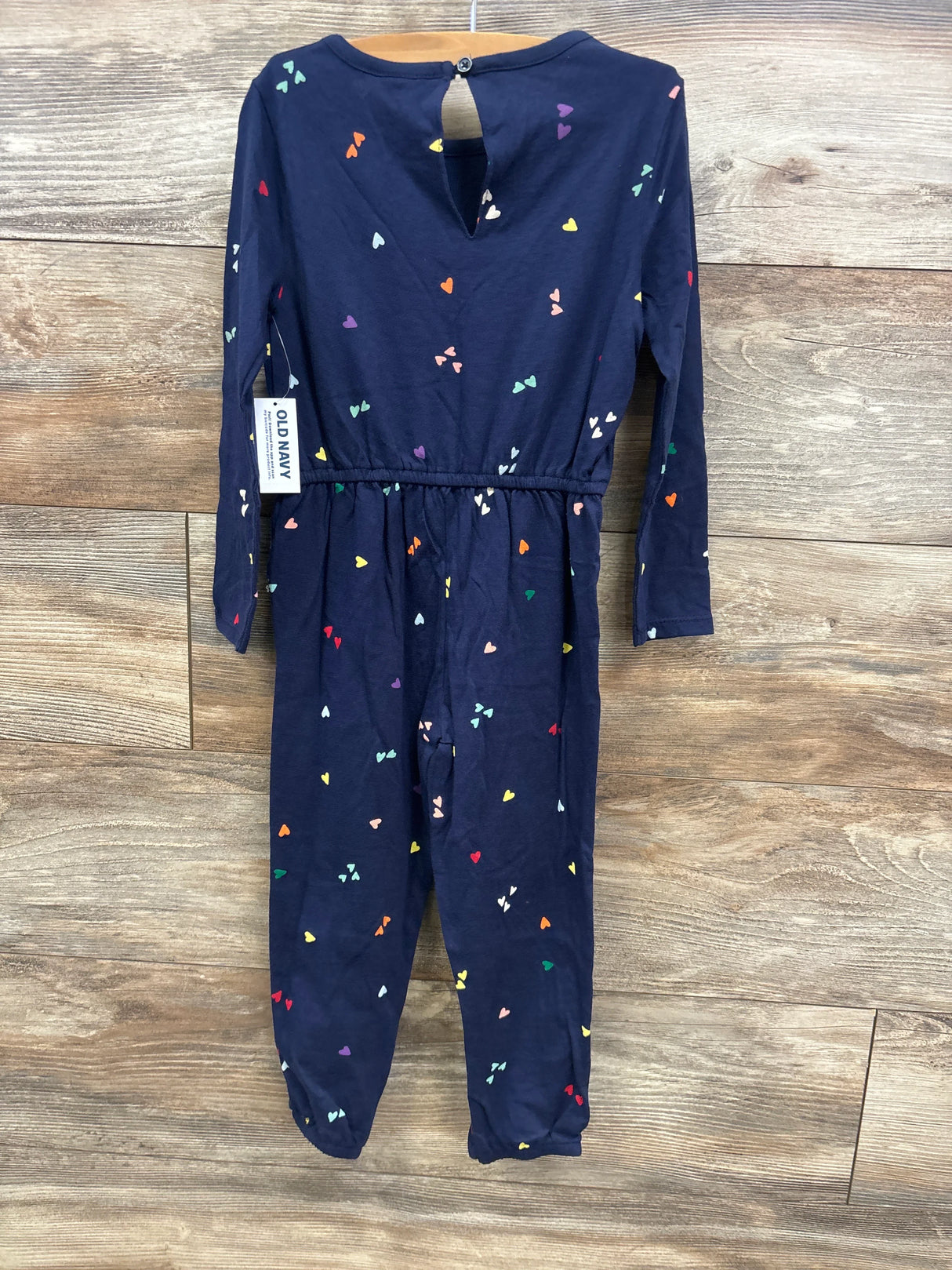 Old Navy navy blue long-sleeve kids jumpsuit with multicolored heart prints hanging on wooden wall