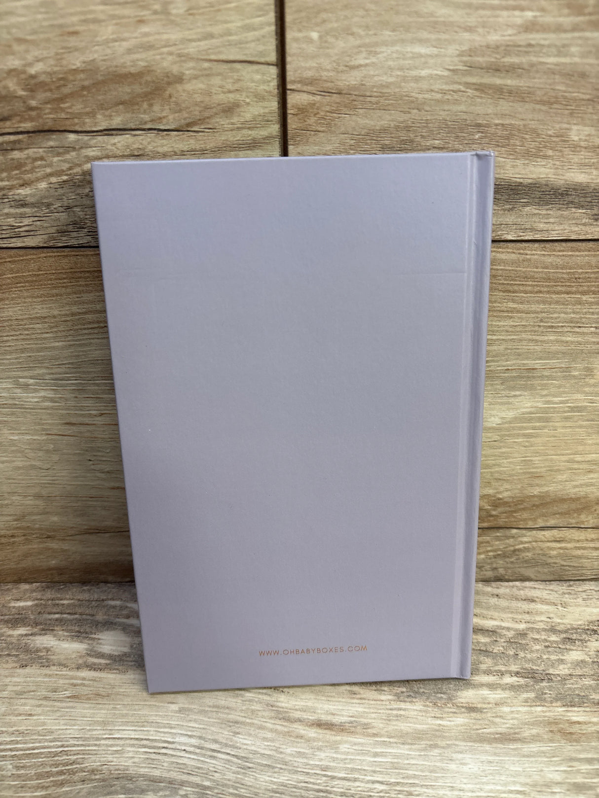 Closed lavender hardback journal with www.ohbabyboxes.com on wooden background