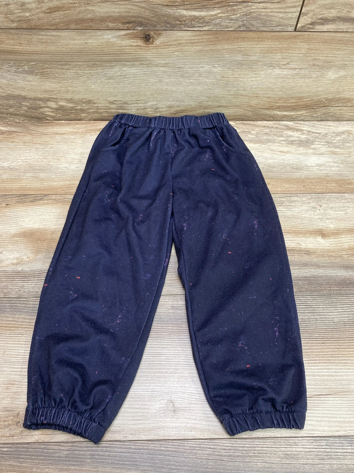 Flat lay of navy toddler jogger pants size 2-3T showcasing elastic waistband and gathered cuffs on wood floor background