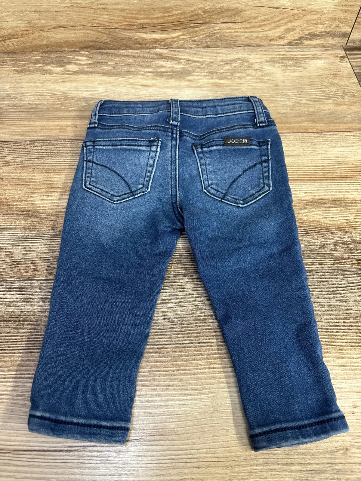 Kids blue denim jeans with back pockets on wood floor, Joe's Jeans label visible