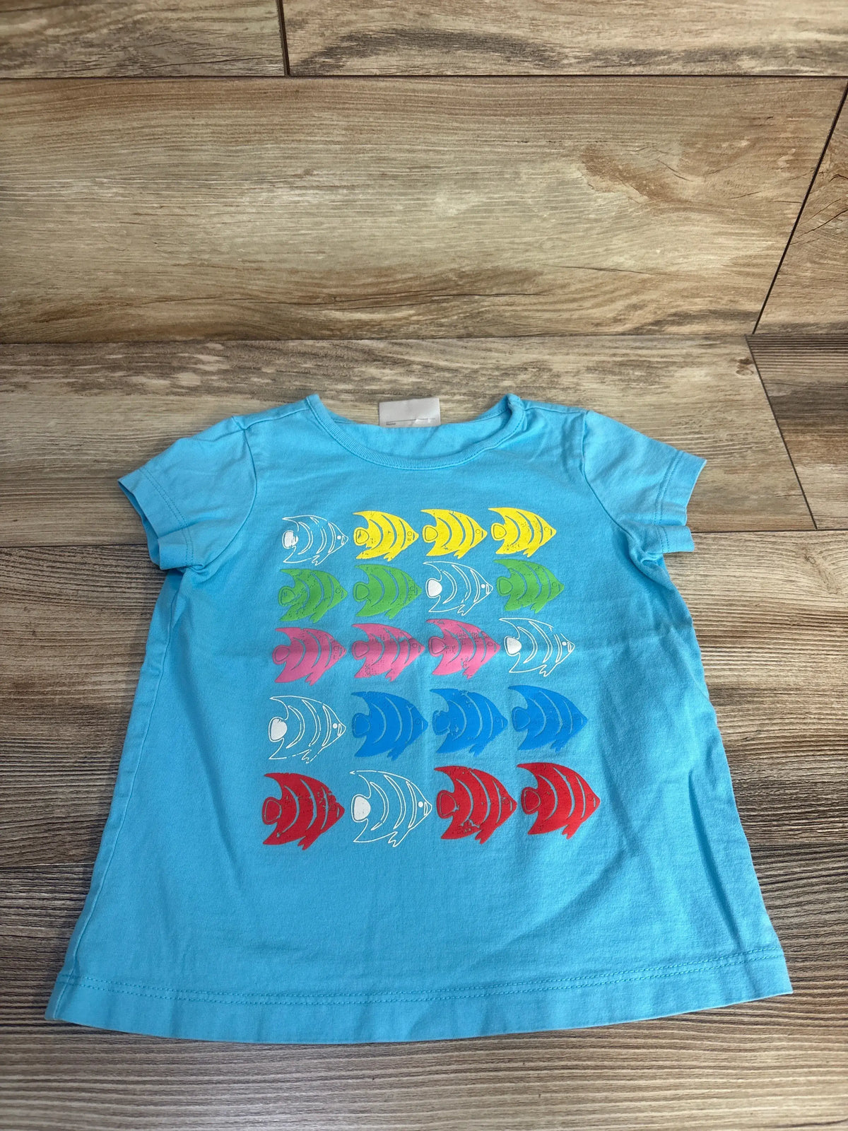 Front view of Hanna Andersson fish print shirt in blue size 4T showcasing short sleeves and rows of fish on a wood floor