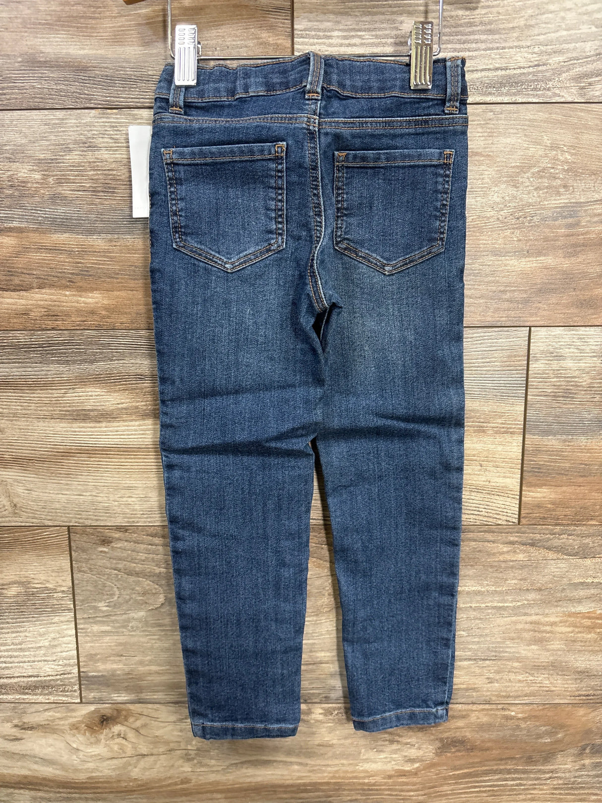 Kids blue denim jeans with back pockets displayed on wooden background