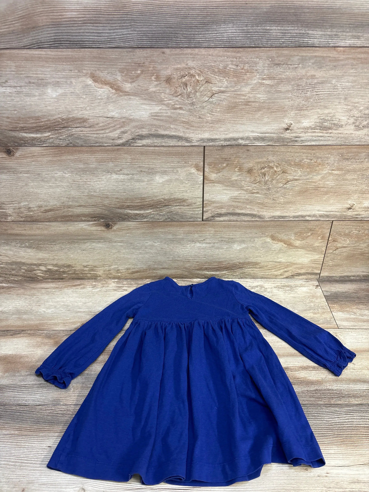 Flat lay of toddler long-sleeve smocked blue dress showcasing gathered skirt and elasticated cuffs on light wood background