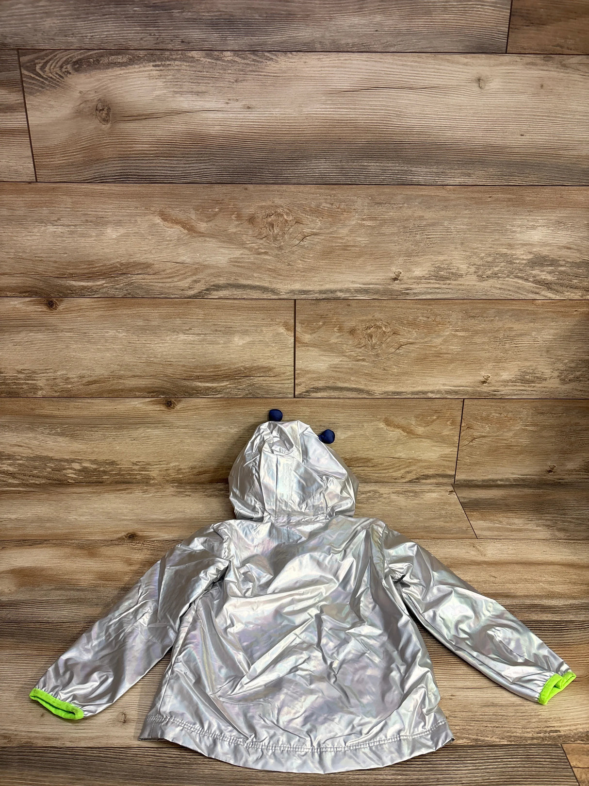 silver reflective children's hooded jacket with blue bear ears and neon green cuff details on wood floor