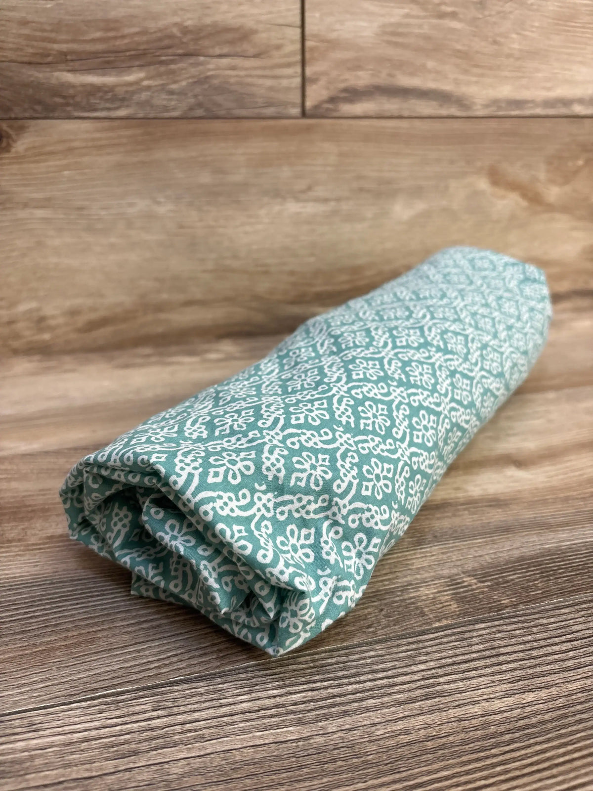 Angled view of Levtex Baby fitted crib sheet showcasing teal green color and white floral medallion pattern on wood background