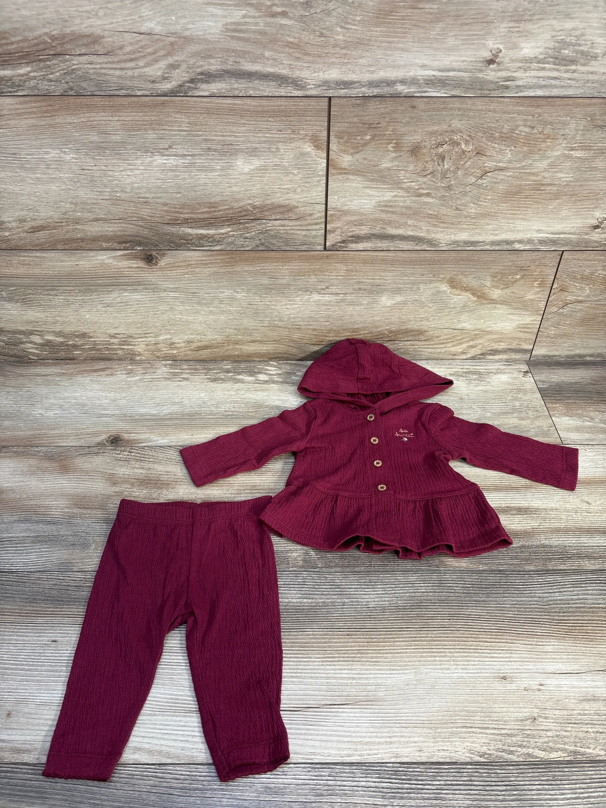 Top view of Carters maroon 2-piece baby outfit showcasing hooded button-up peplum top and coordinating pants on wood floor