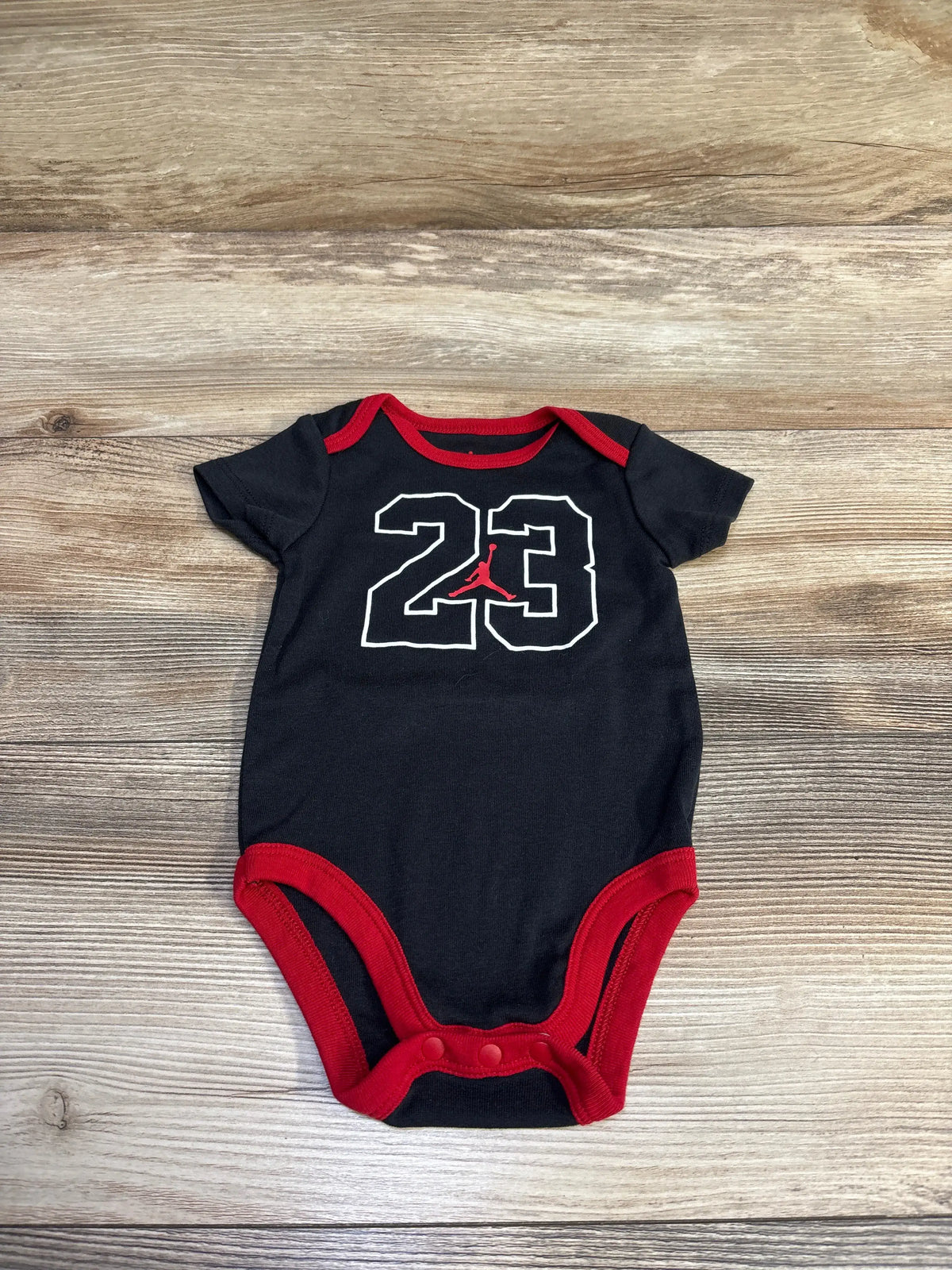 Black Me n Mommy To Be bodysuit with red trim and white number 23 on a wood background
