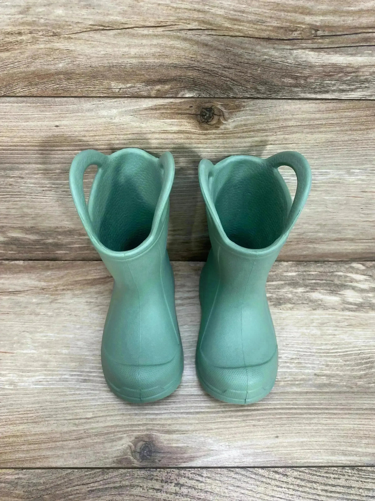 Front view of BEARPAW Toddler EVA Rain Boots Green sz 3c showcasing sage green molded boots with side pull-on handles on wood plank floor
