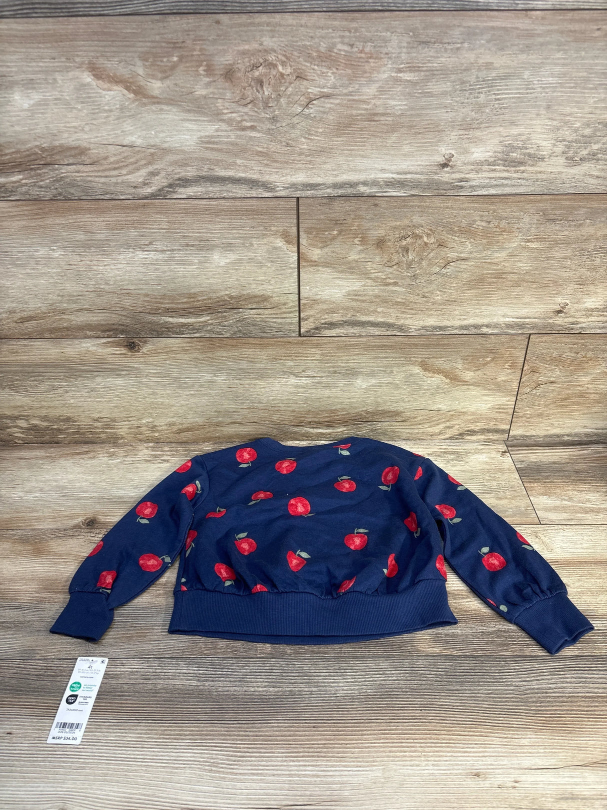 Navy blue kids sweater with red apple print, size 4T, laid on wood floor