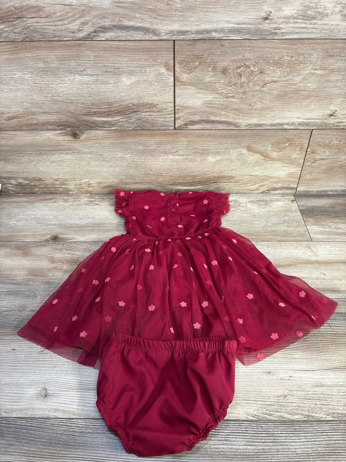 Flat lay of maroon Daisy Fuentes tulle dress with matching bloomers showing puff sleeves and flower details on wood floor