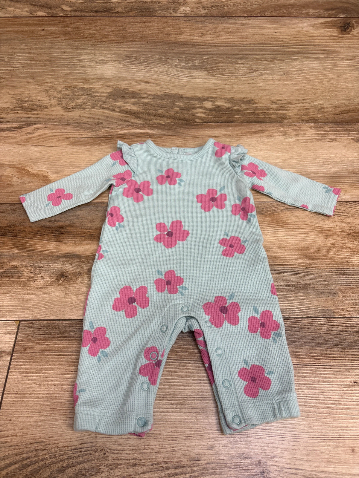 Flat lay of blue Just One You waffle knit coverall with pink floral print, long sleeves, and snap closures on wood