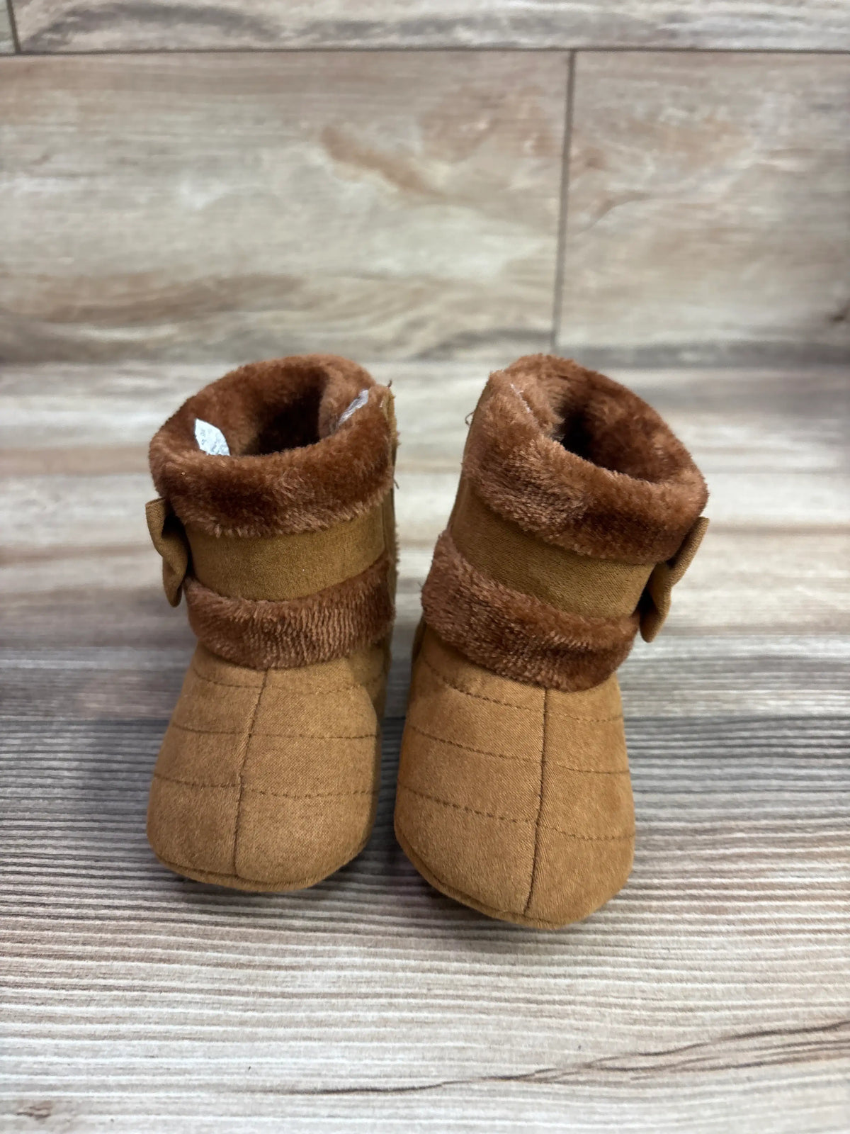 Front view of CRYBOKO brown faux-fur soft-sole boots, size 4/5C, with fur cuffs and side bows on wood