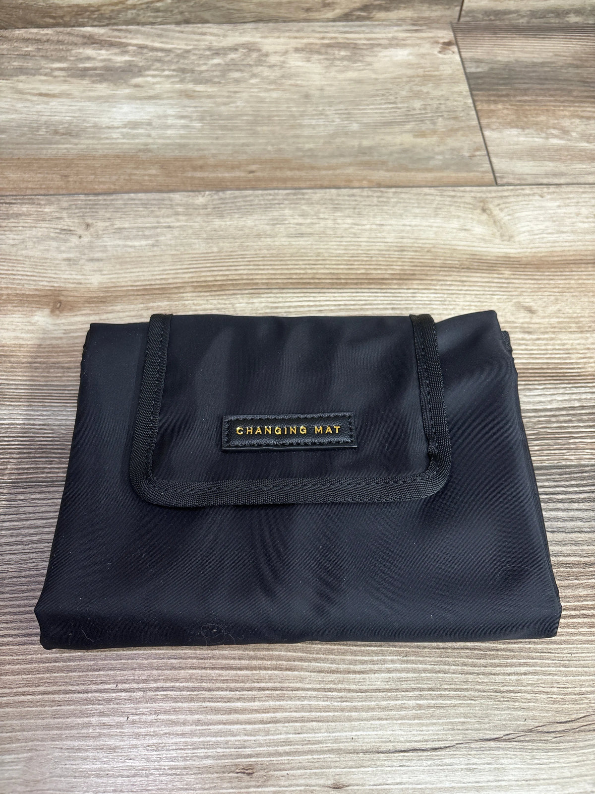 Front view of Katie Loxton portable baby changing mat showcasing its folded black design on a wood-grain surface