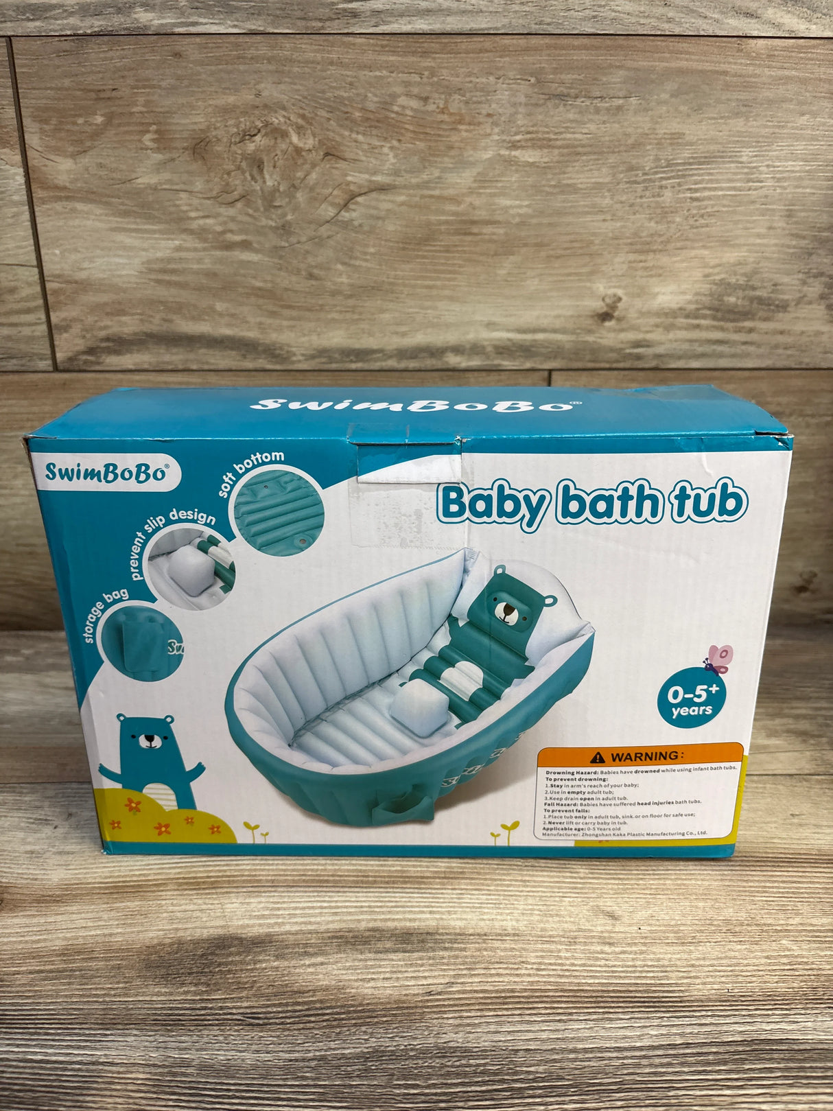 Front view of inflatable baby bath tub showing teal bear-shaped backrest and small inflatable seat on packaging against wooden floor background