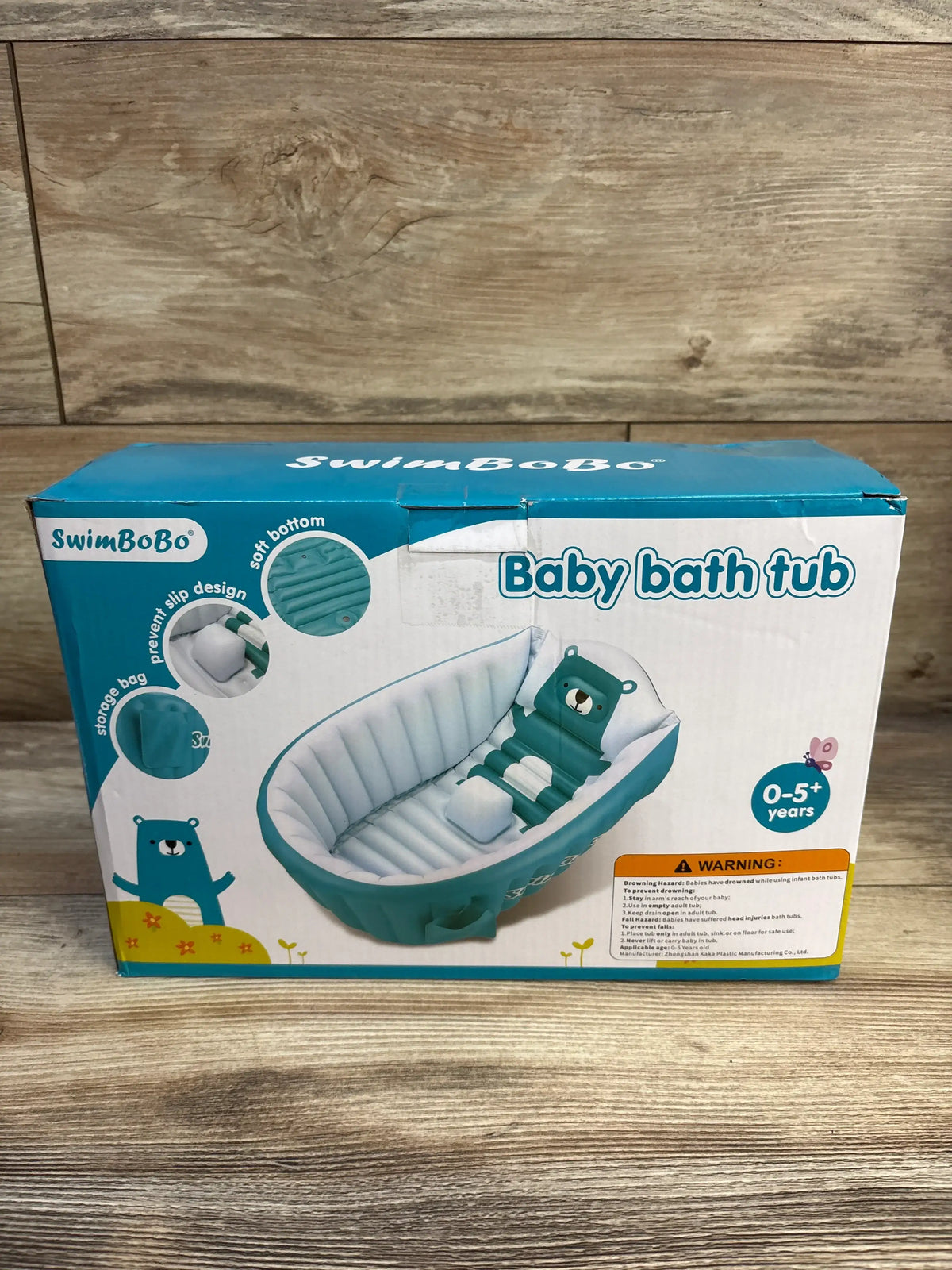 Front view of inflatable baby bath tub showing teal bear-shaped backrest and small inflatable seat on packaging against wooden floor background