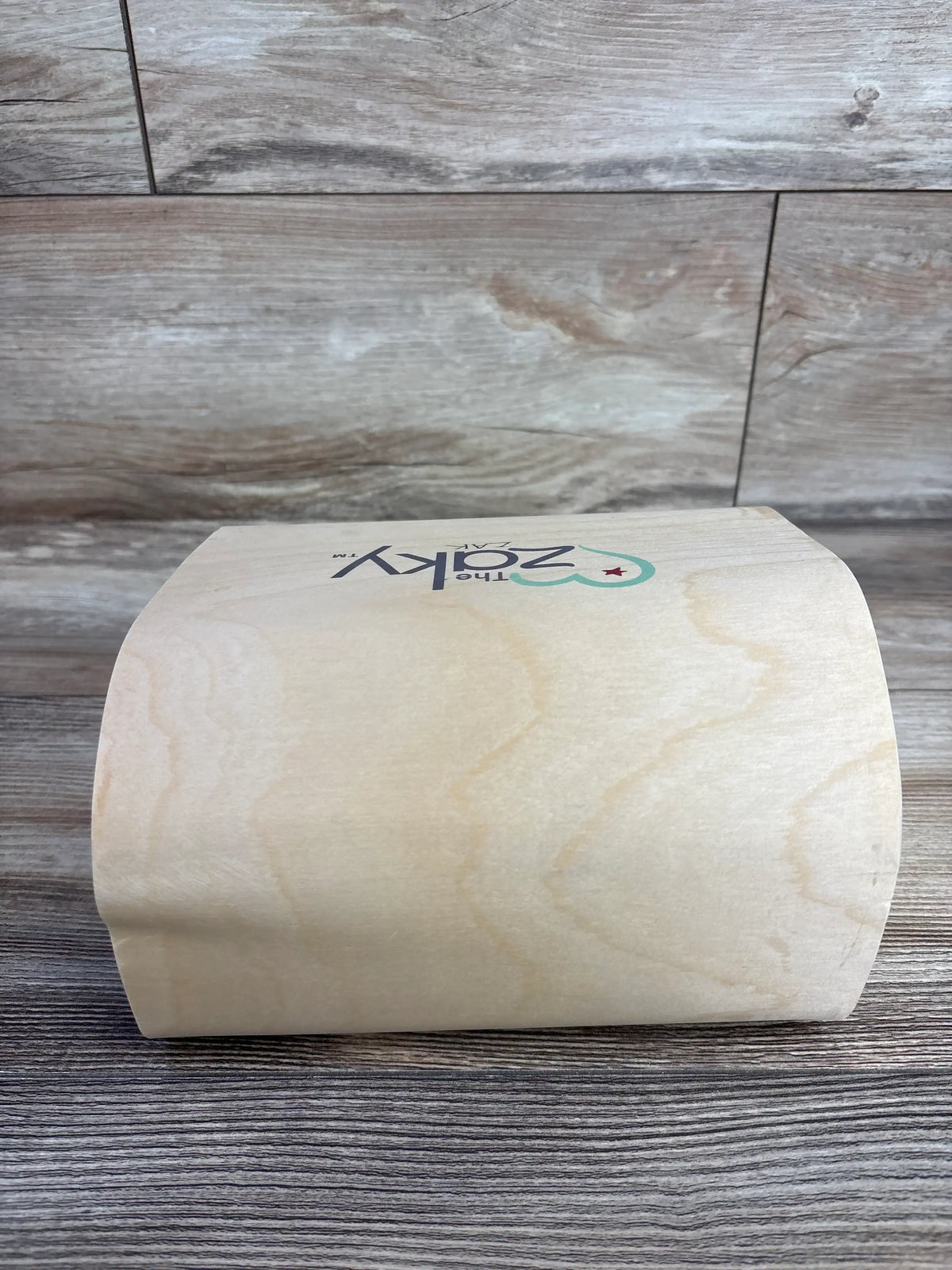 Front view of The Zaky curved wooden arch toy showcasing smooth natural wood finish and printed logo with wood plank background
