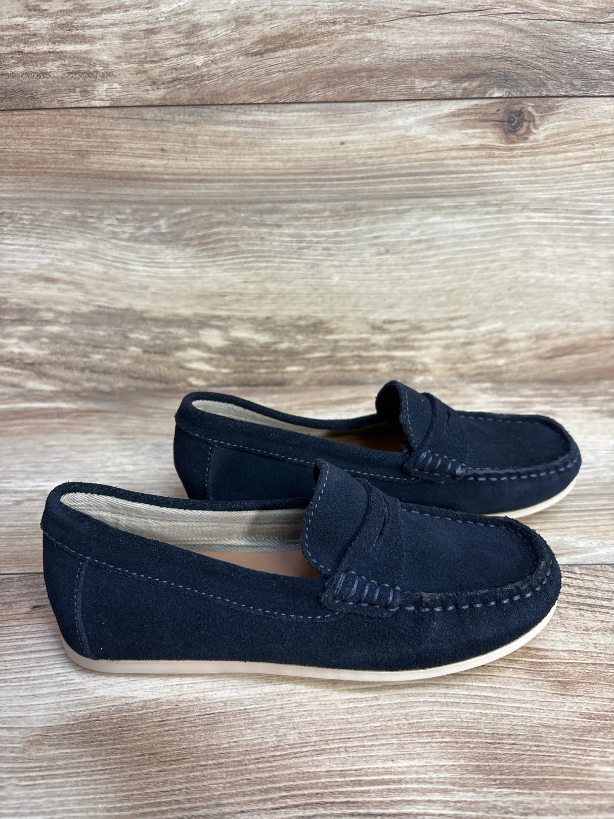 Black suede loafers with white stitching on wood floor background