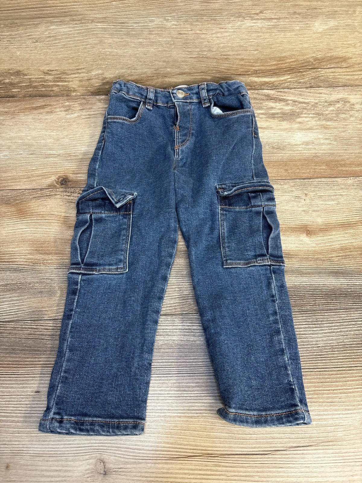 Kids denim cargo pants with side pockets, laid flat on wood floor