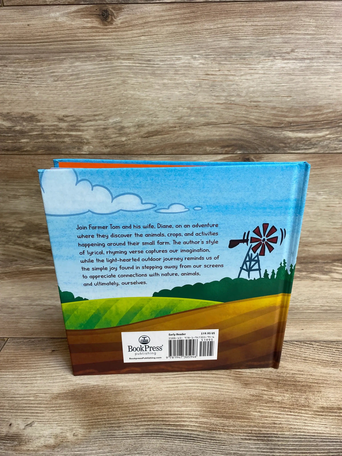 Back view of Farmer Tom Hardcover Book showcasing illustrated farm scene with windmill, green fields, and a short blurb about Farmer Tom and his wife Diane