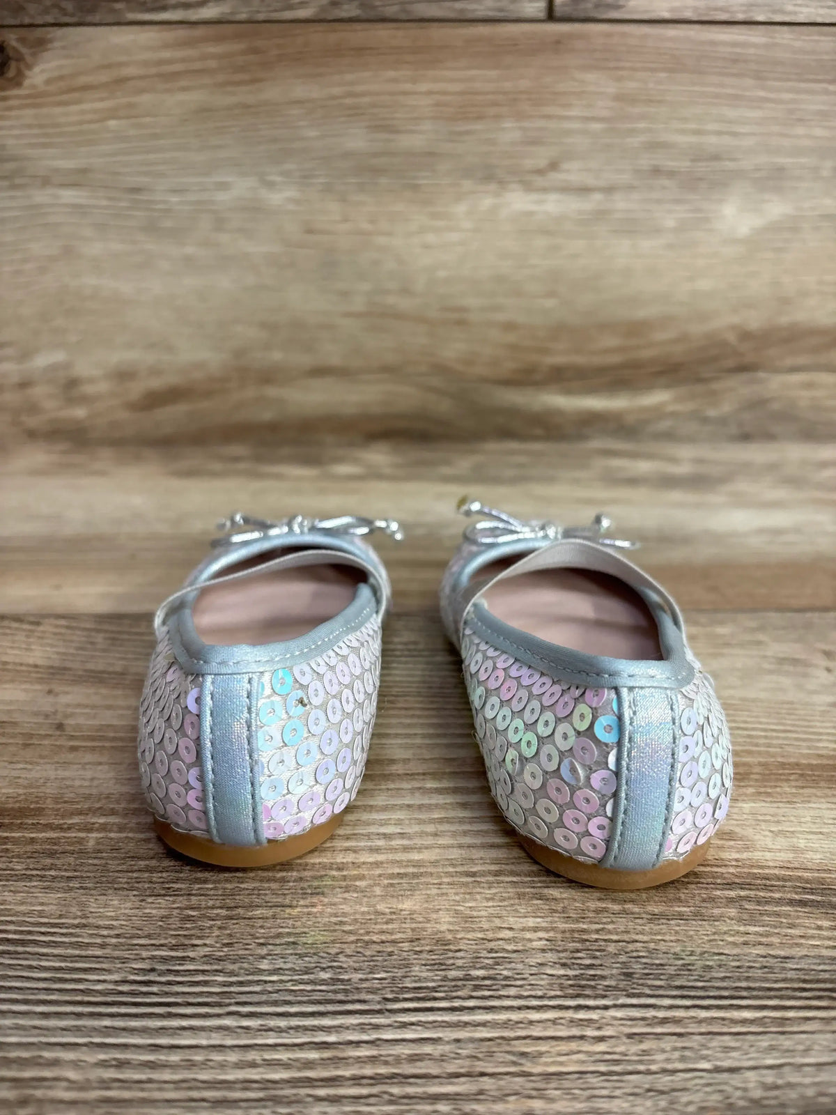 Pair of children's silver sequin ballet flats with bows on wooden surface