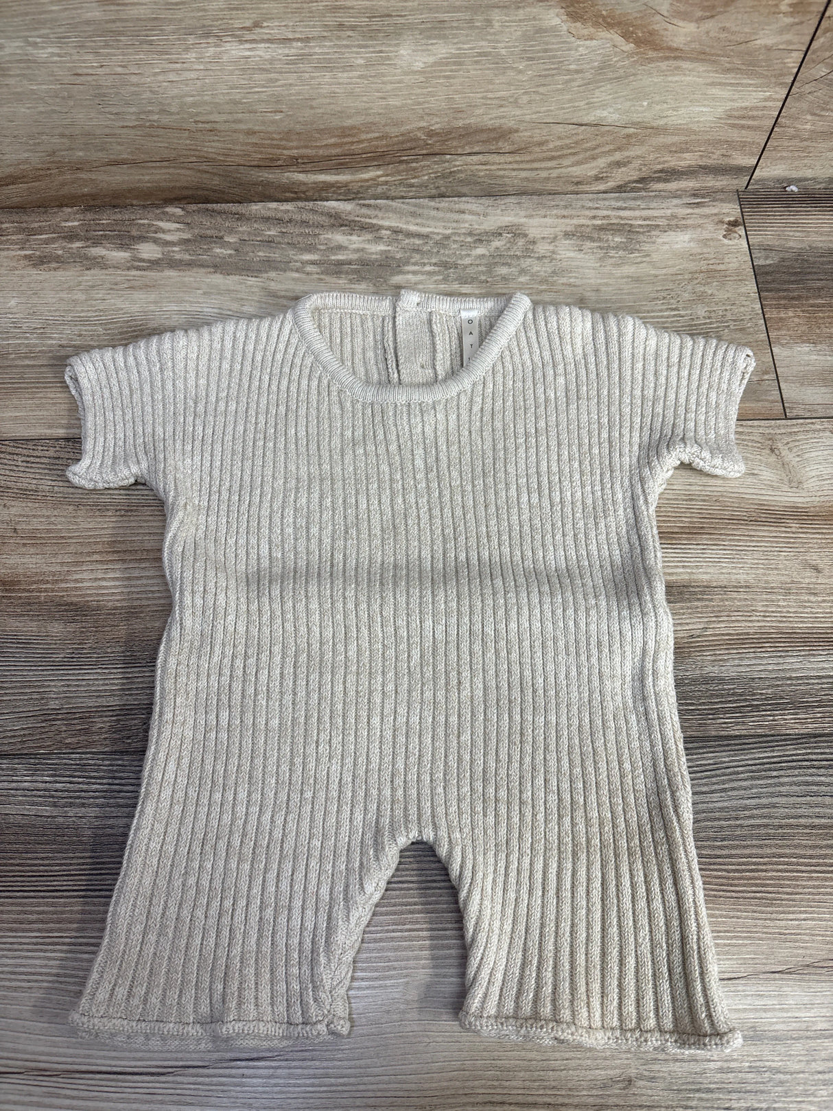 Beige ribbed knit baby romper with short sleeves laid on wood floor
