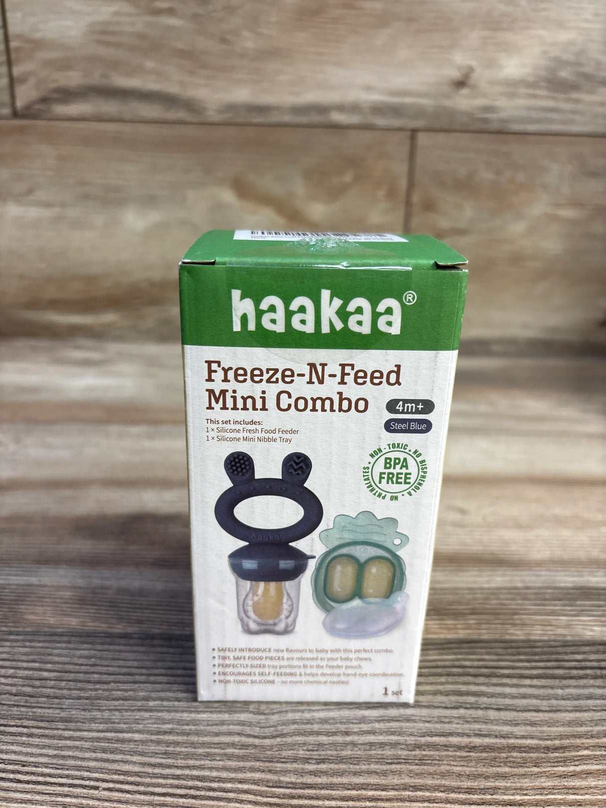 Front view of Haakaa Freeze-N-Feed Mini Combo box showcasing steel-blue silicone feeder and mini nibble tray with wood plank background