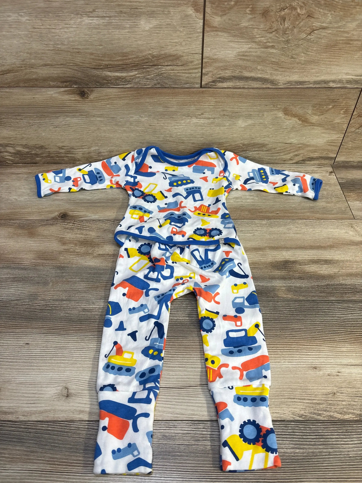 Flat lay of OETEO convertible sleeper romper showcasing multicolor construction vehicle print and blue trim on wood floor