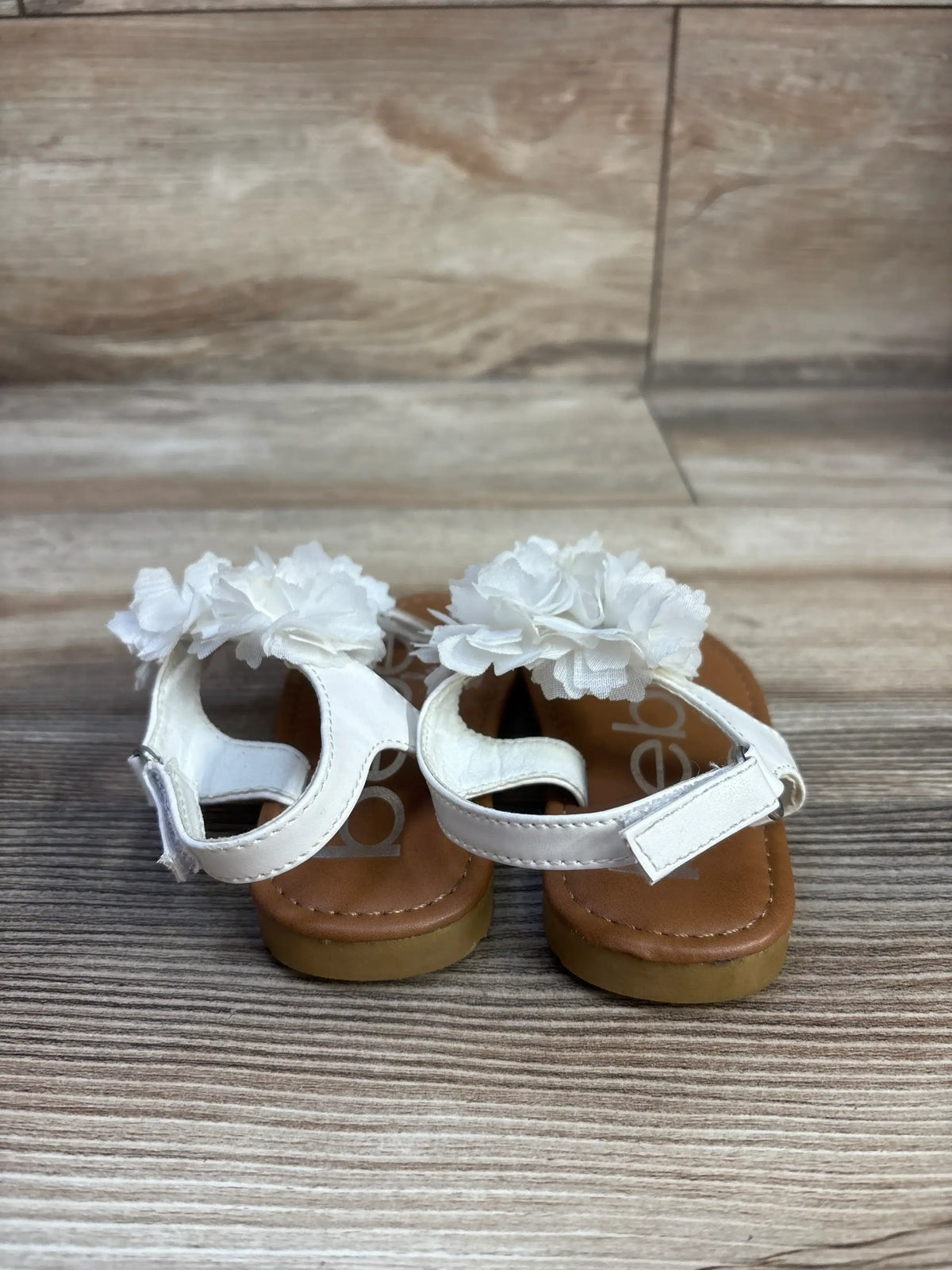 Front view of Bebe white chiffon flower sandals showcasing floral accents and ankle straps on a wood-grain surface