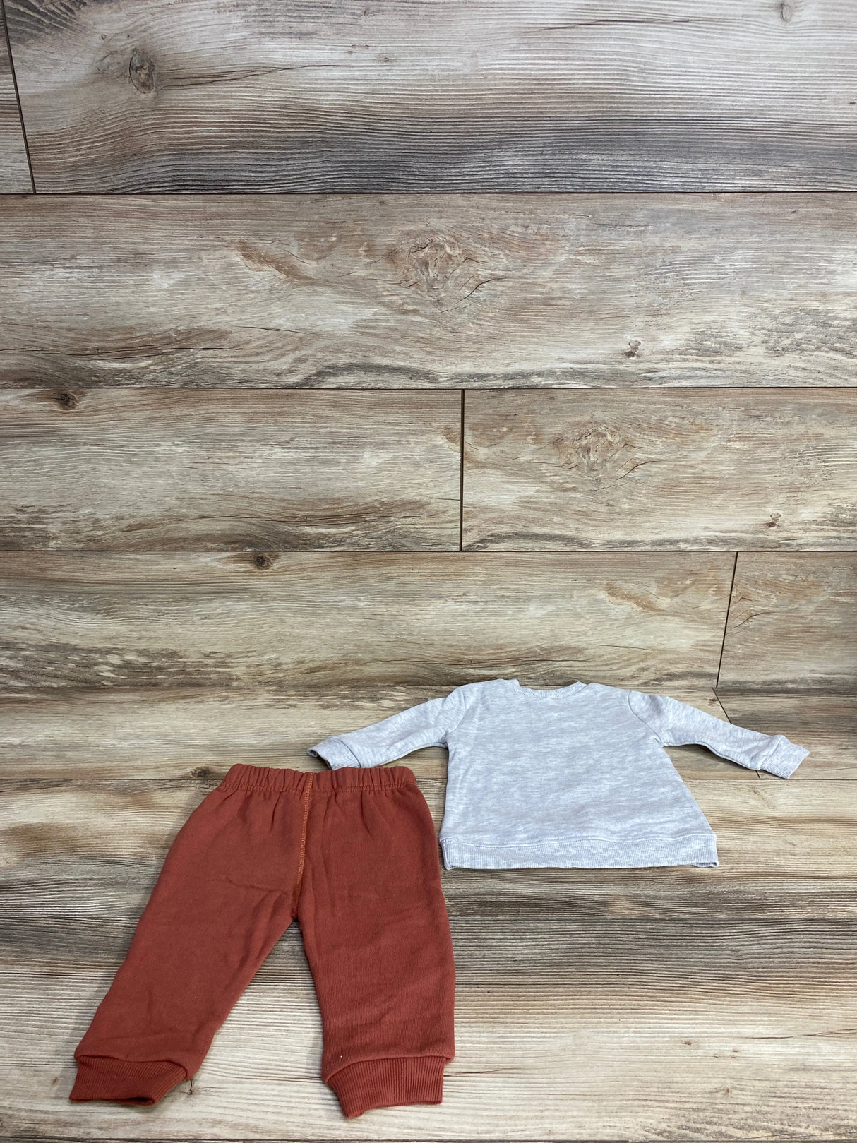 Children's two-piece outfit with rust-colored pants and light gray long-sleeve shirt on wood floor