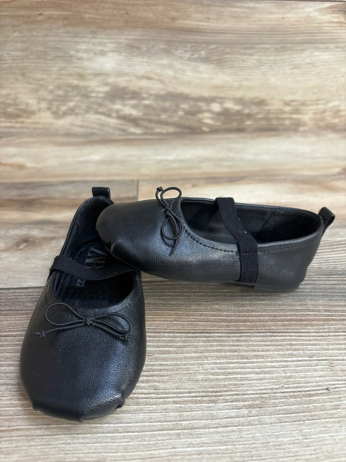 Three-quarter view of Zara black leather ballet flats showcasing bow detail and elastic strap on wood plank floor