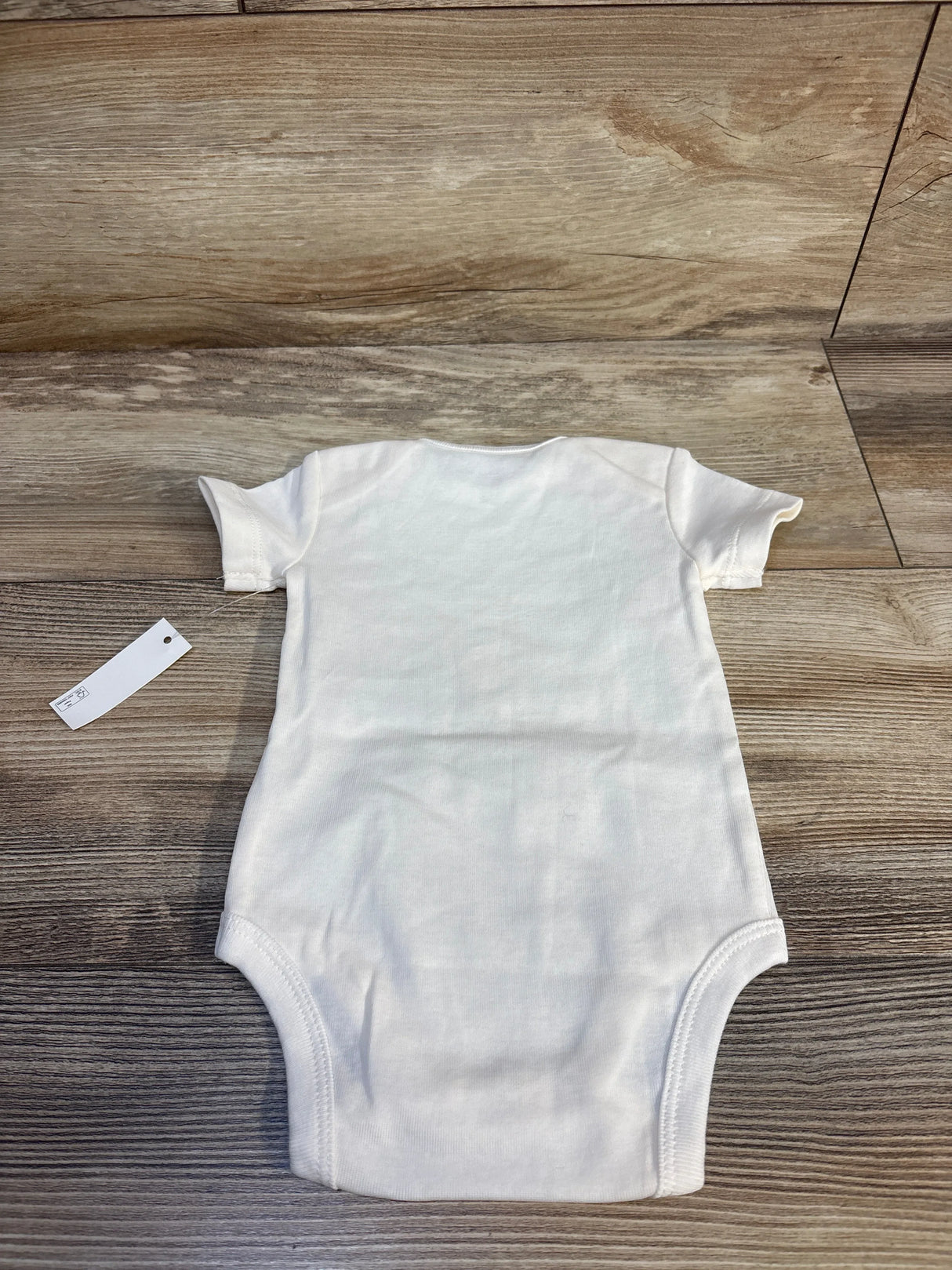Back flat-lay of Amazon Essentials ivory baby bodysuit, size 3-6M, showing crew neck, short sleeves, and ribbed leg openings on wood background
