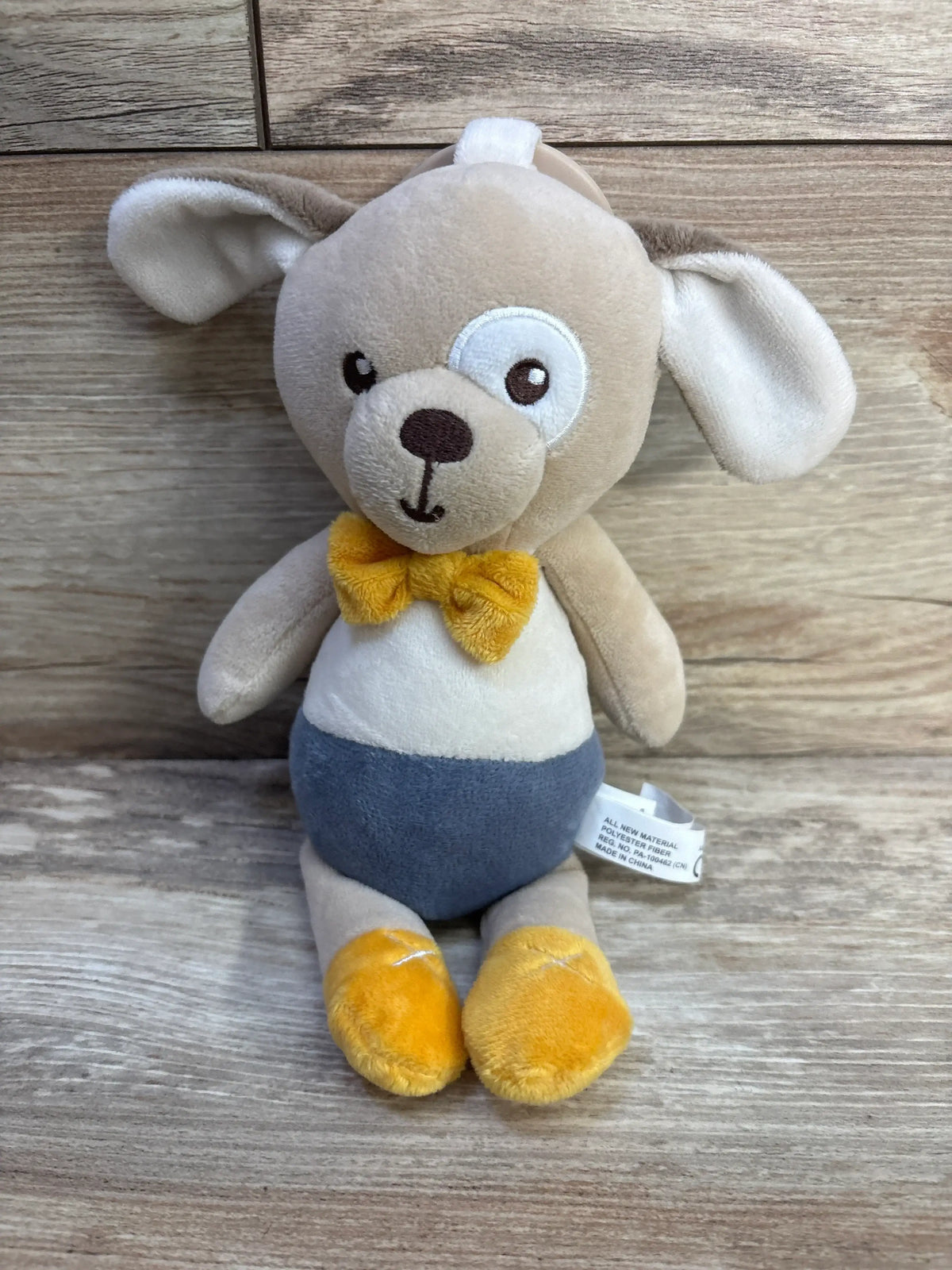 Front view of DreamGro Stroller Plush Dog Toy showing its loop attachment, yellow bow tie, and blue lower body on wood