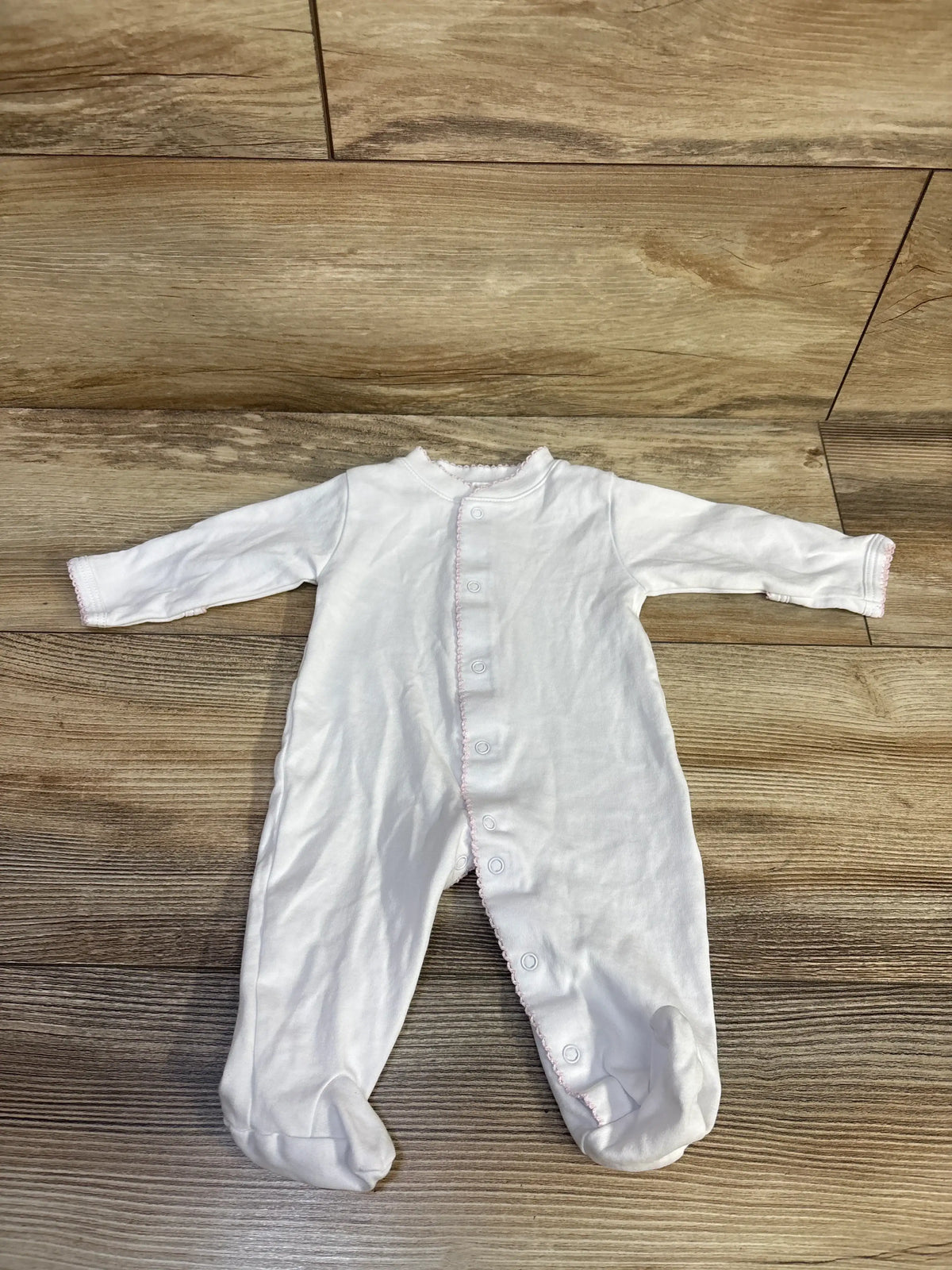 Front view of Kissy Kissy white newborn snap sleeper showcasing long sleeves and footed legs with a wood floor background