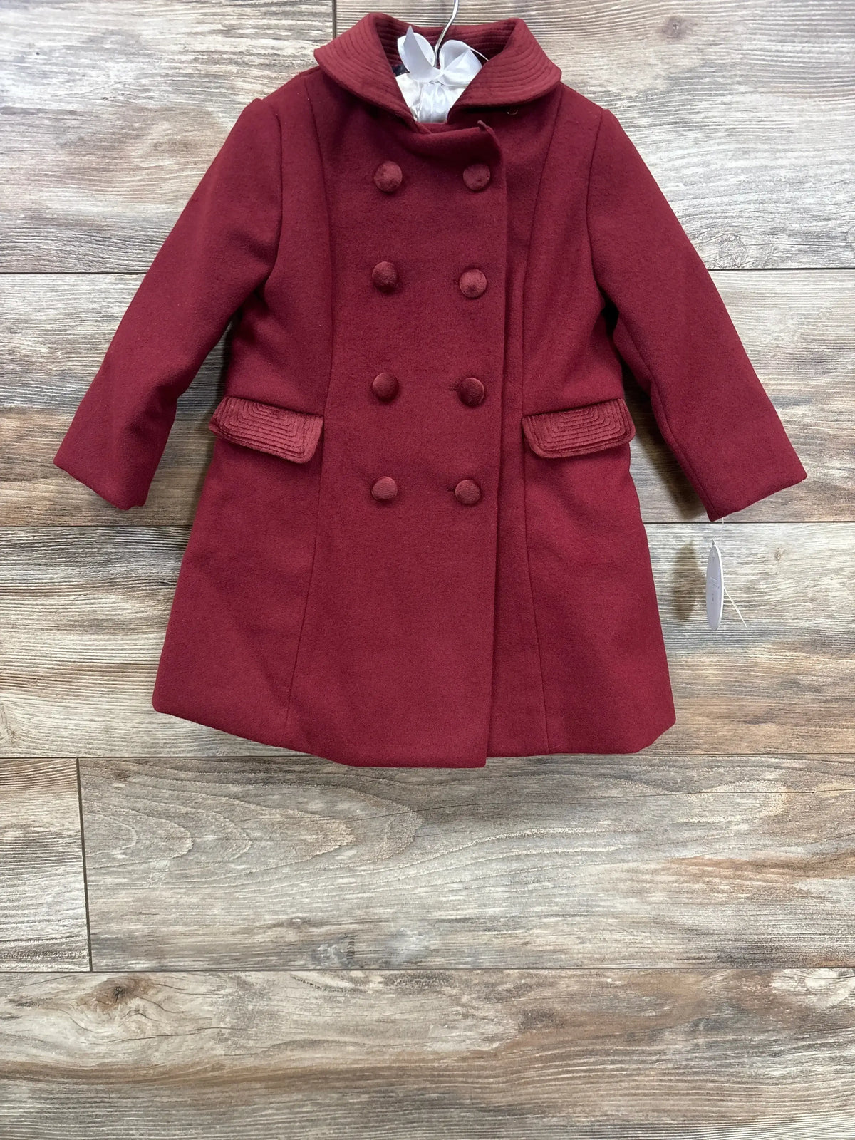 Burgundy double-breasted girls' wool coat with buttons and collar on wooden floor