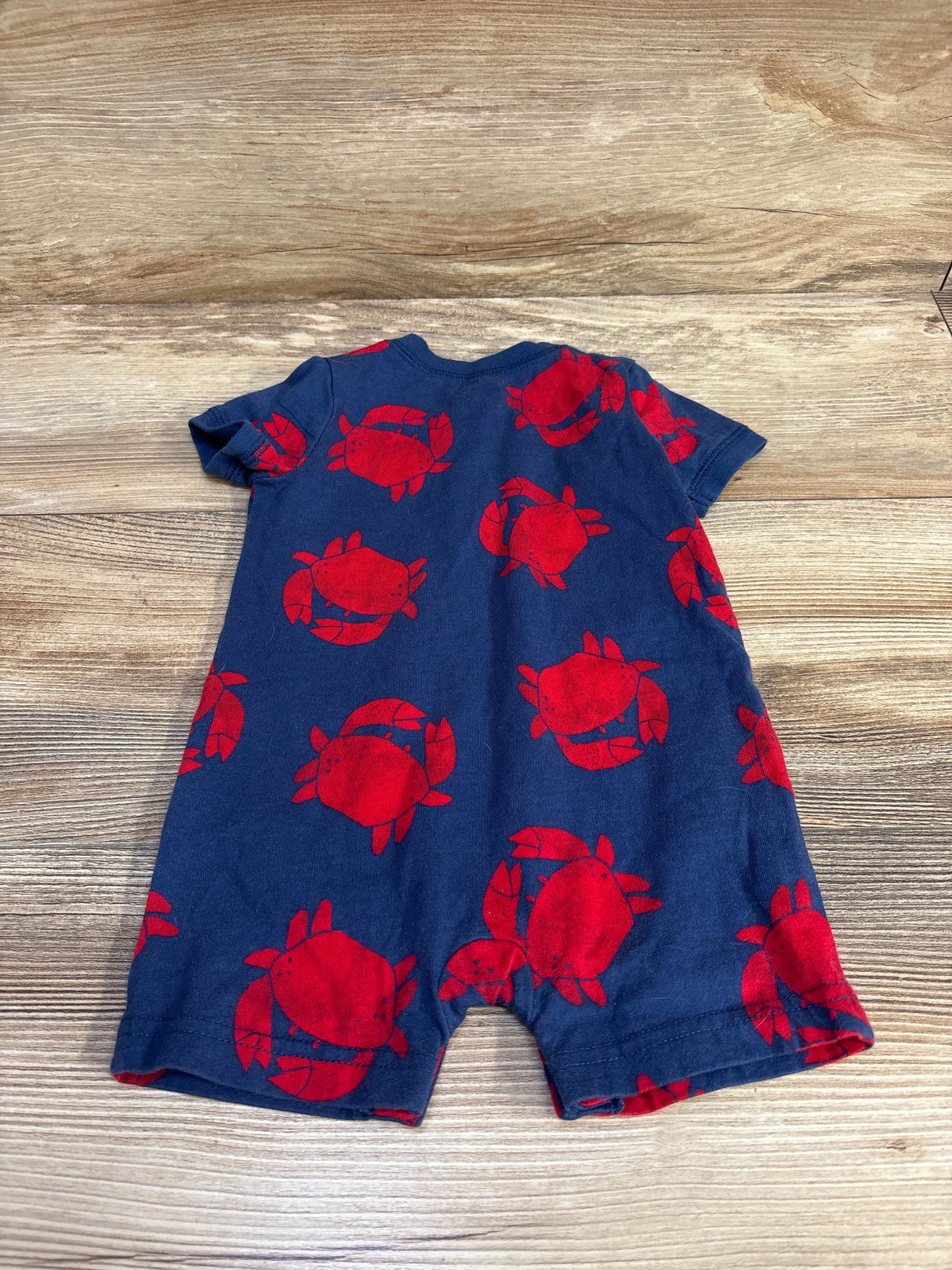 Navy blue baby romper with red crab print on wood background