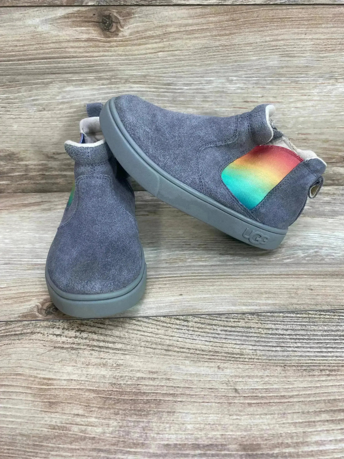 Angled view of UGG Hamden II suede toddler sneakers size 11C showcasing rainbow side elastic and grey sole on wood background
