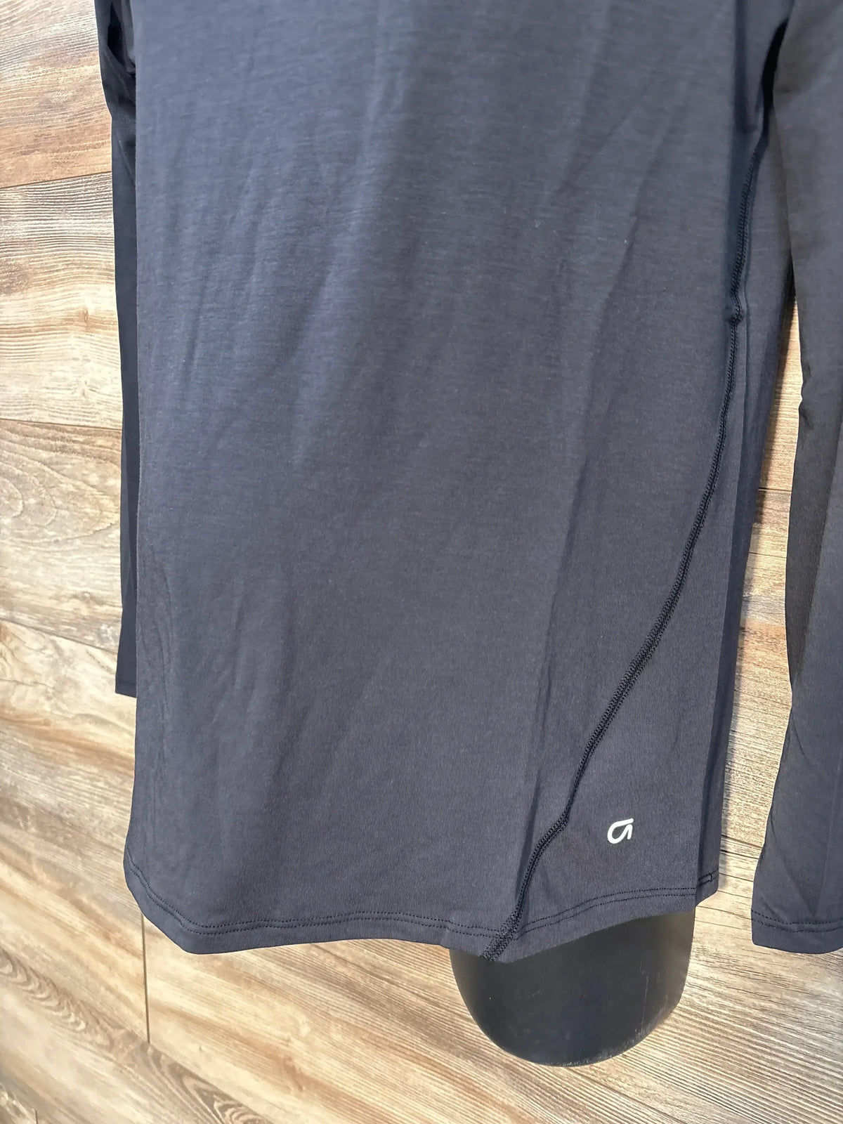 Front view of GapFit Breathe maternity long-sleeve tee in true black showing curved side seam and small white logo above hem on wood background
