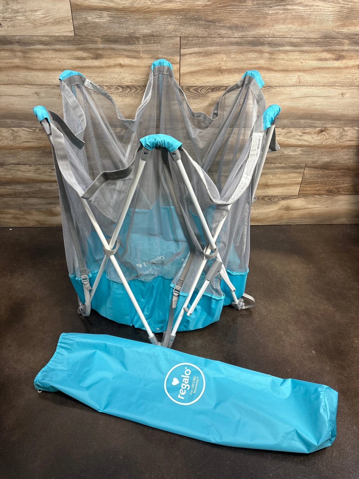 Regalo portable play yard with mesh sides and blue travel bag on wood floor
