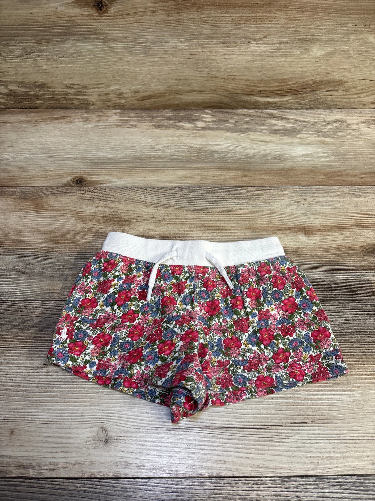 Flat lay of toddler terry shorts showing pink and red floral print, white elastic drawstring waistband on wood background