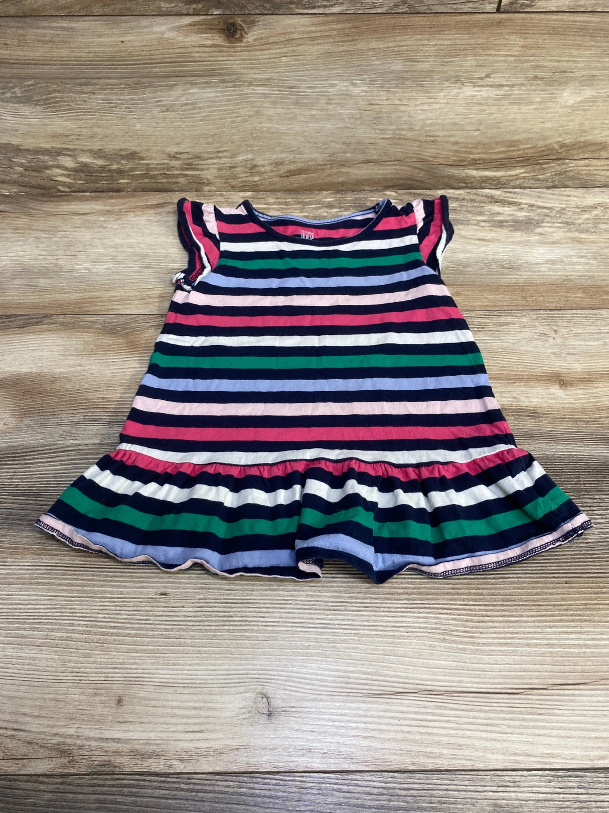 Flat-lay of Baby Gap striped peplum toddler shirt (navy multicolor) showcasing ruffled hem and cap sleeves on wood background