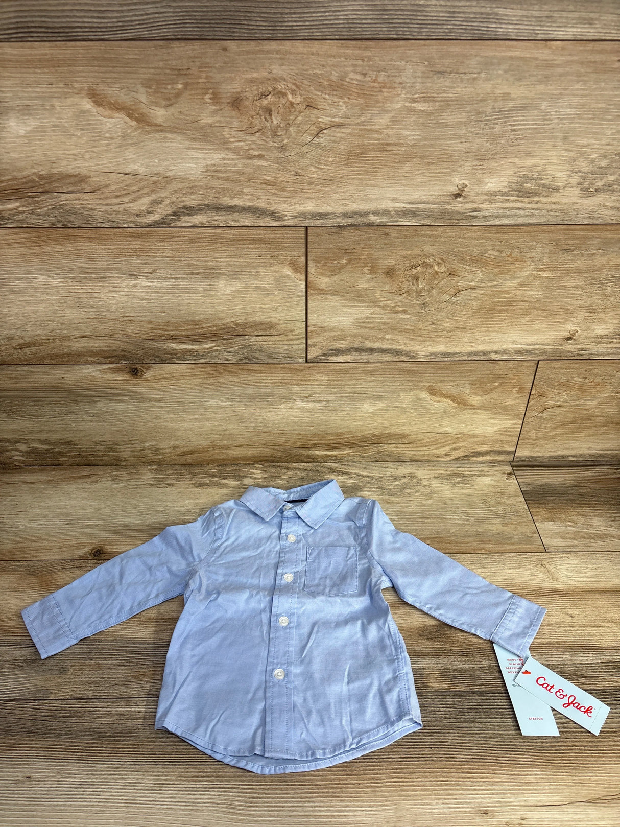 Light blue long-sleeve baby shirt with front buttons and Cat & Jack tag on wood background