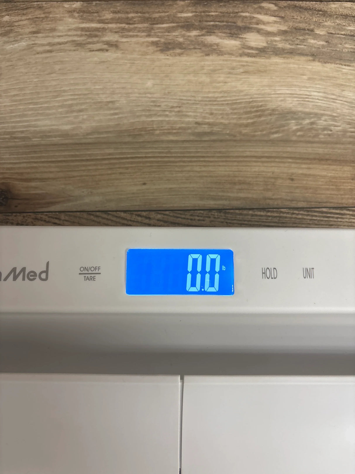 Digital baby scale with blue backlit display reading 0.0 lb on wood surface