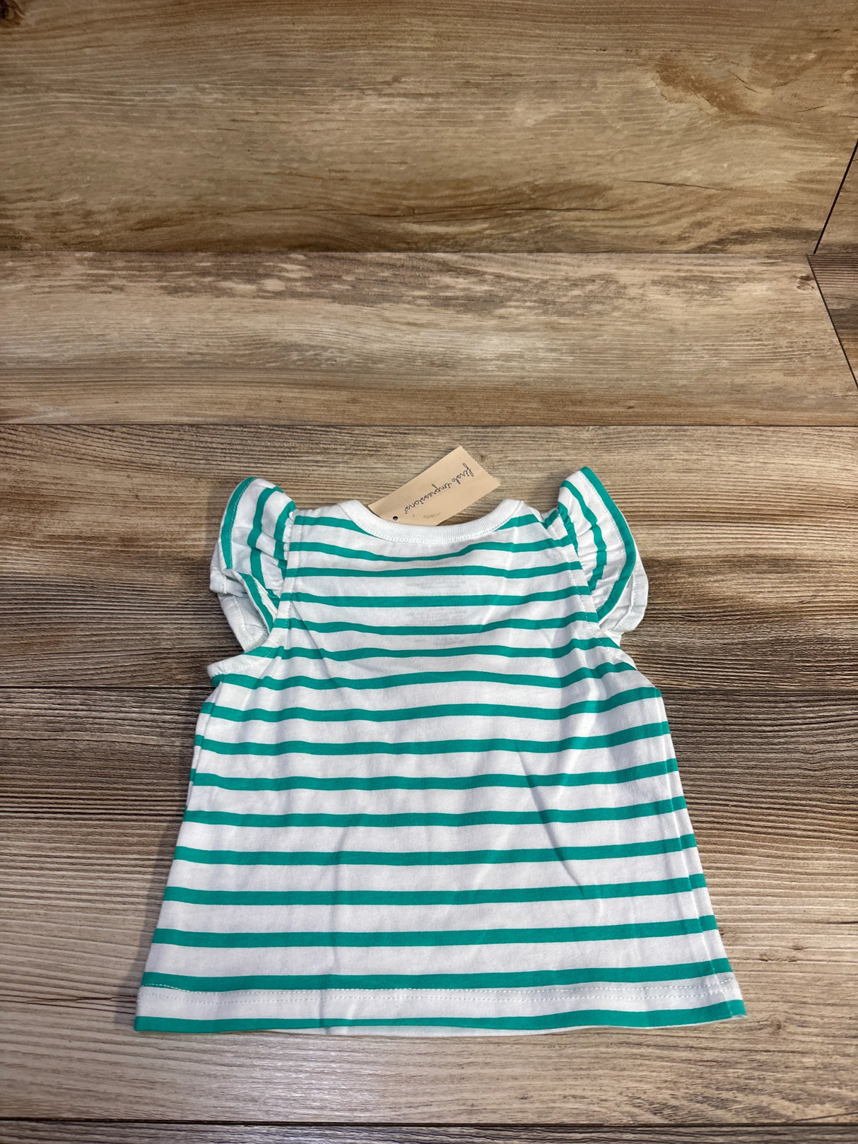 Back view of baby striped shirt showing green and white horizontal stripes and flutter sleeves on wood background