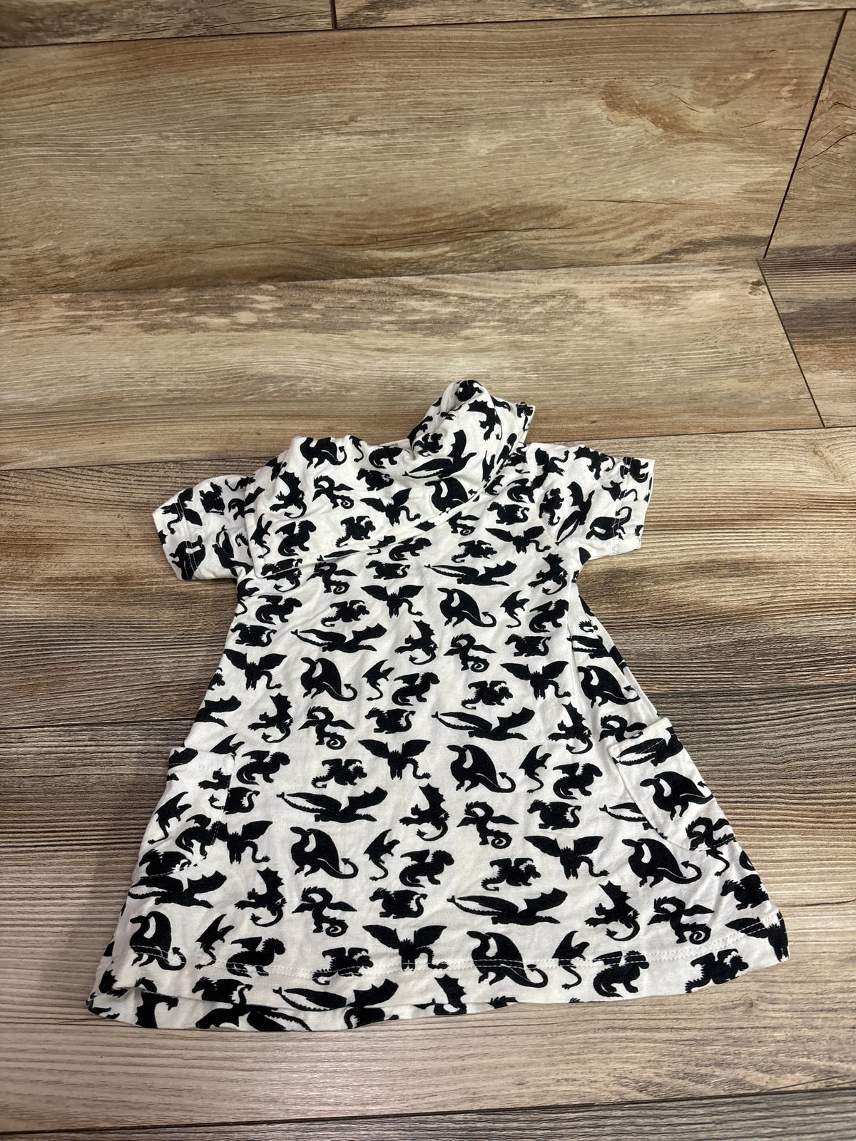 White Kate Quinn bamboo baby dress with black dragon print on a wood floor