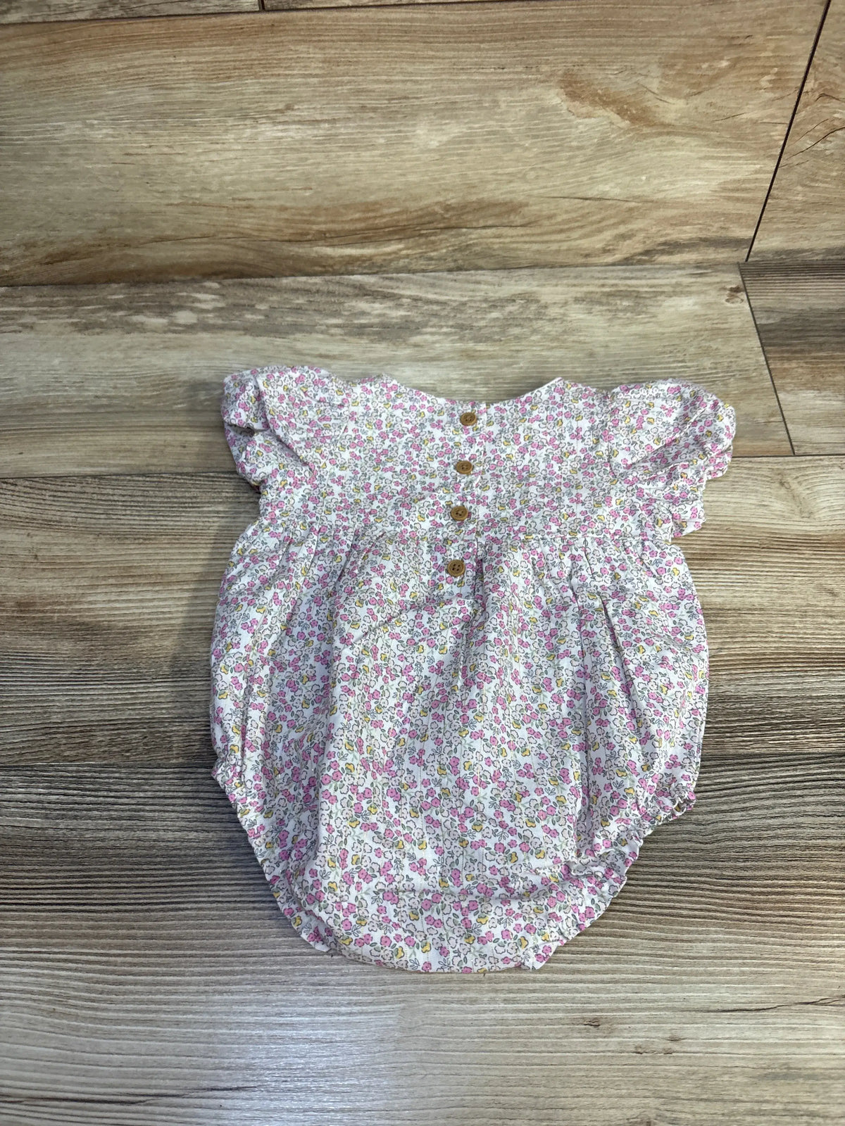 Top view of Child Of Mine white floral bubble romper showcasing gathered legs and snap closures on a wood floor
